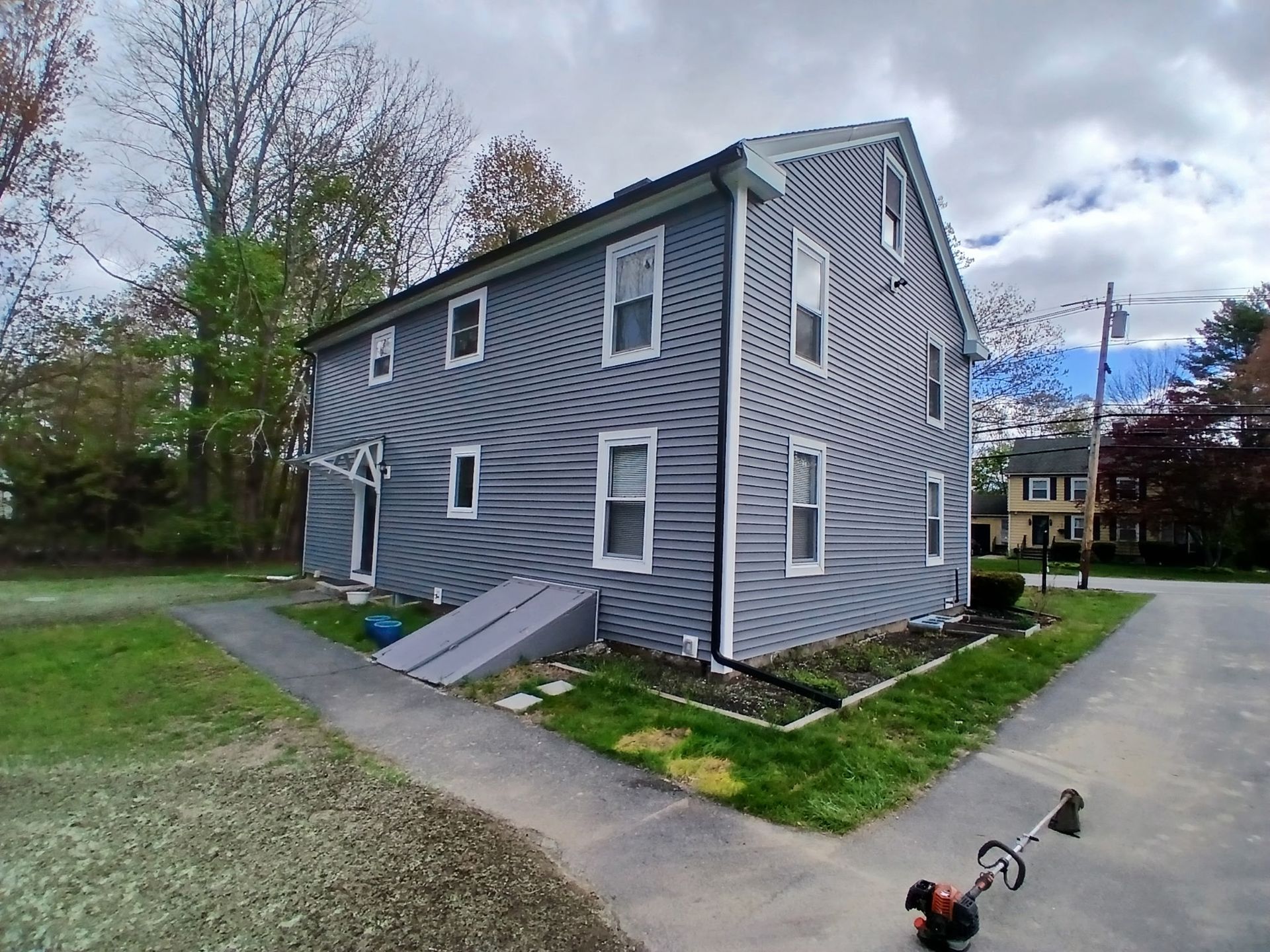 Gray two-story house with white trim, sloped roof, and a small front ramp beside a driveway.