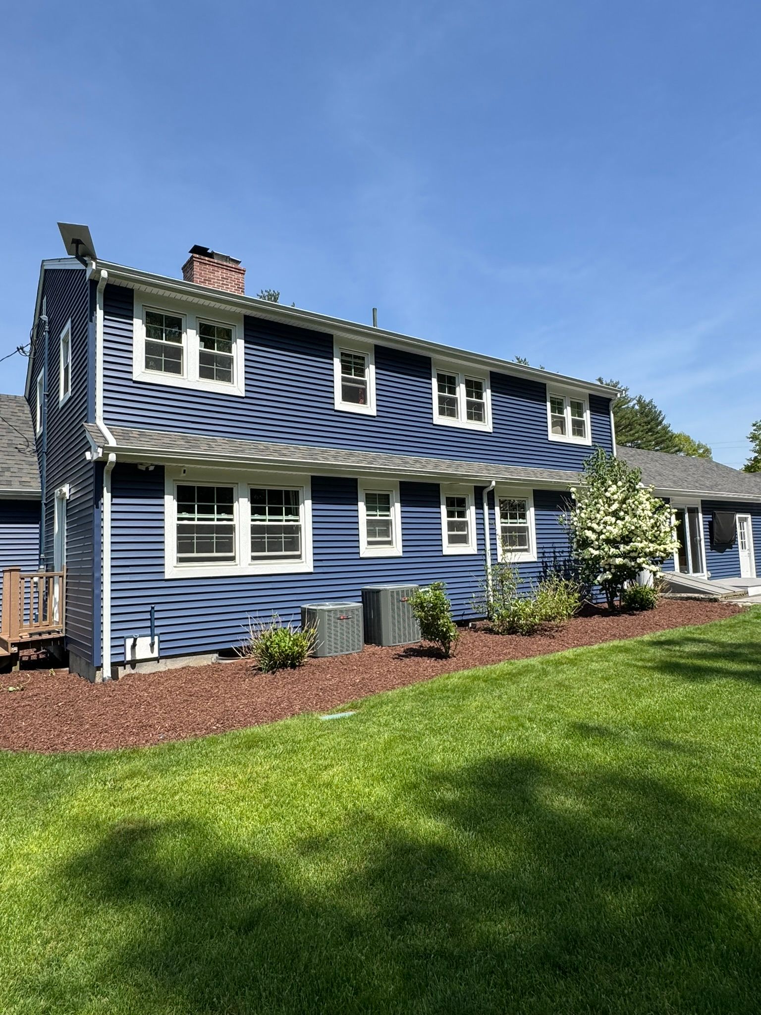 Blue two-story house with white trim and a green lawn under a bright blue sky