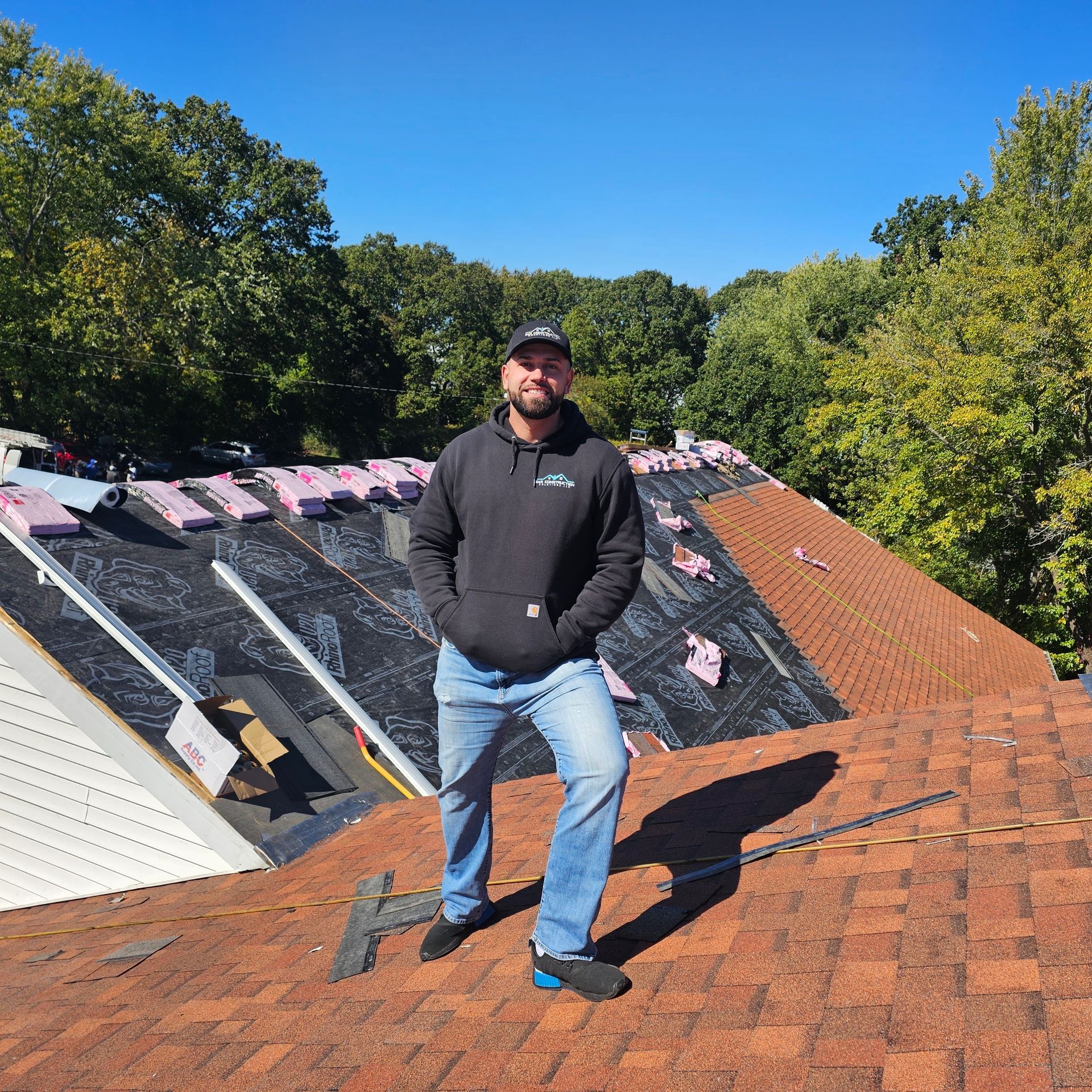 Person standing on a roof under repair beside black underlayment and red shingles
