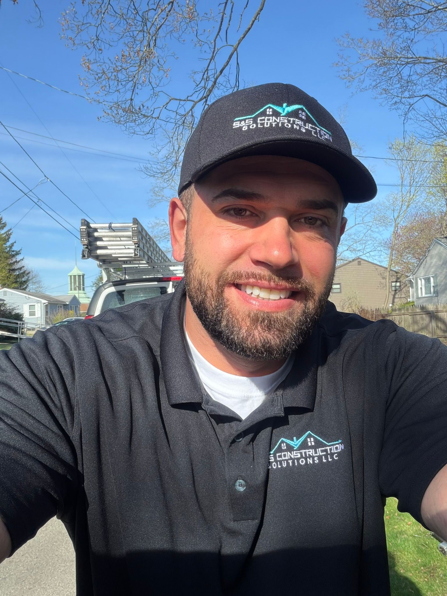 Smiling man in a black cap and polo outdoors under a blue sky
