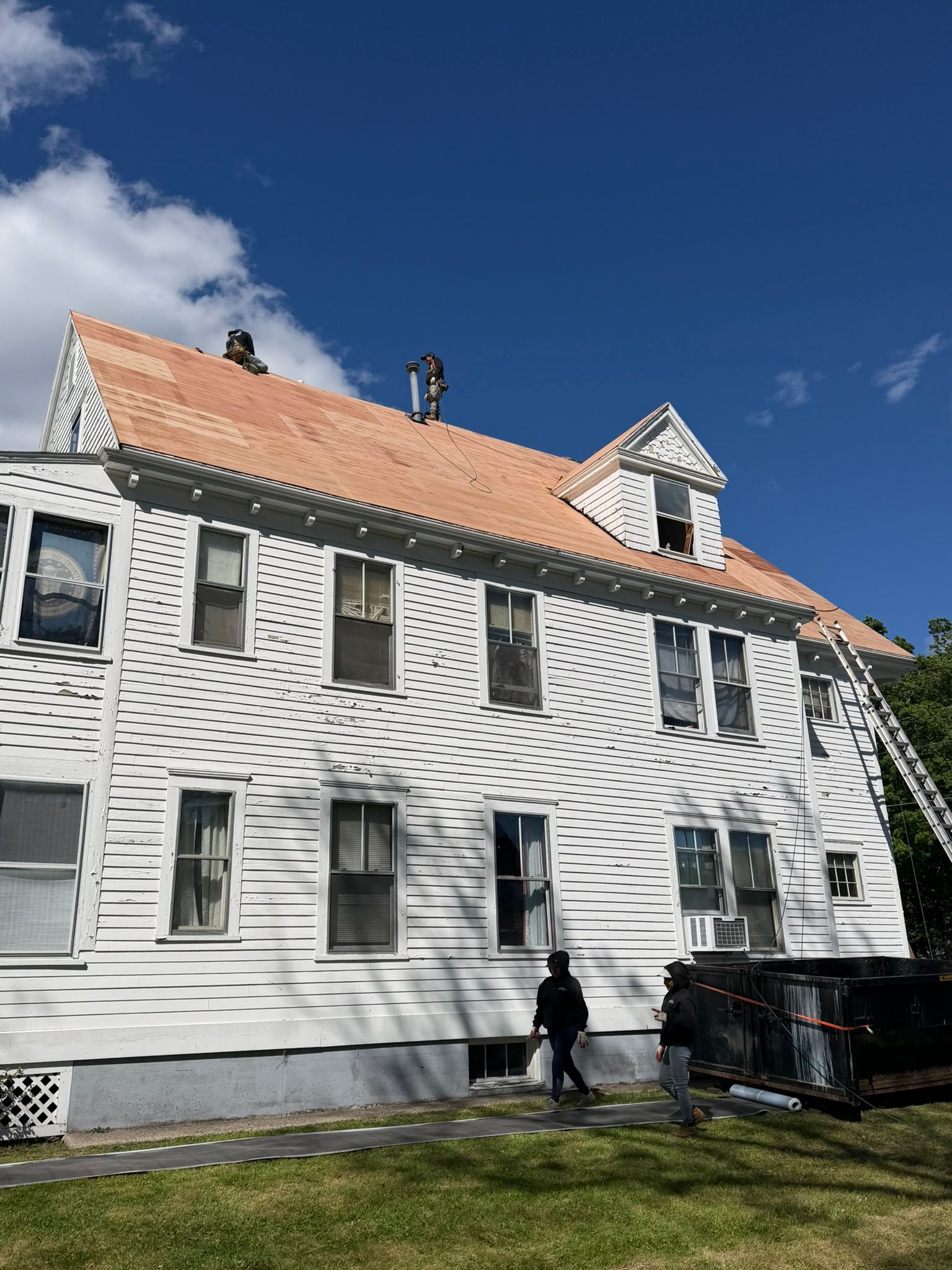 White clapboard house with orange roof under a blue sky, with a person walking beside it