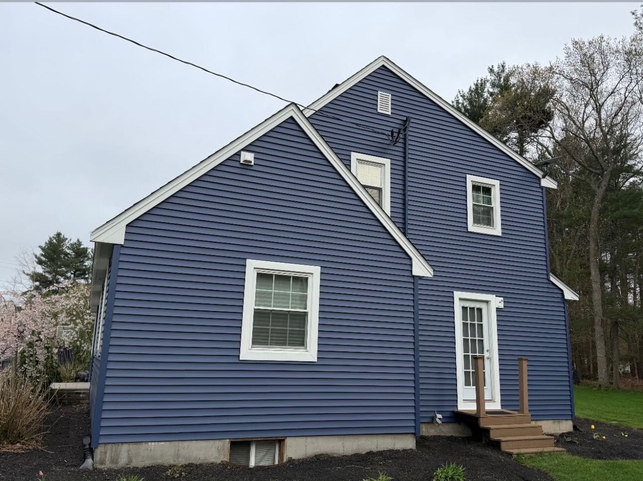 Blue two-story house with white trim and a small front porch under an overcast sky