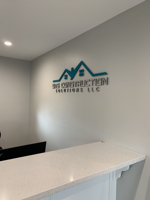 Office reception desk with teal construction company logo on a gray wall
