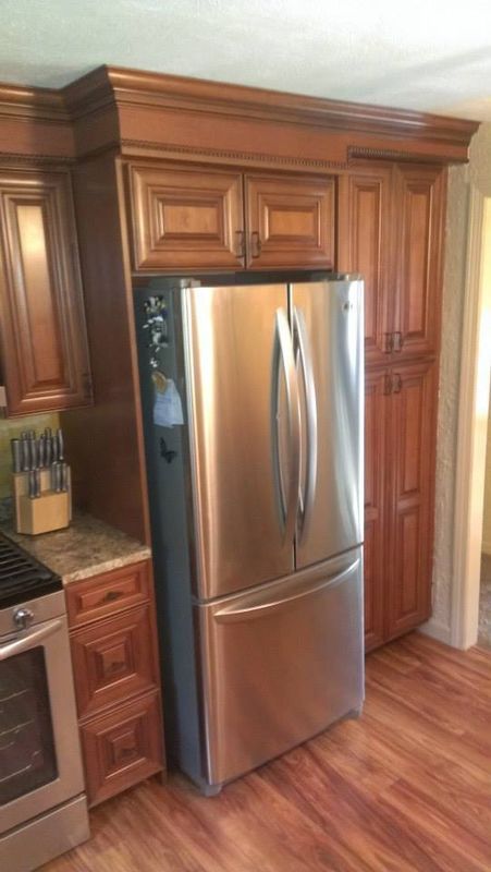 Stainless steel refrigerator framed by warm wood kitchen cabinets and hardwood floor