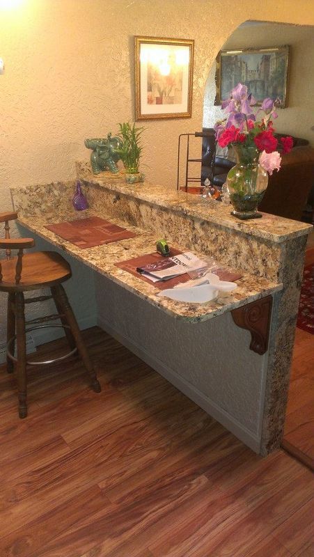 Kitchen counter with granite top, flowers, papers, and a stool in a warm-toned home interior