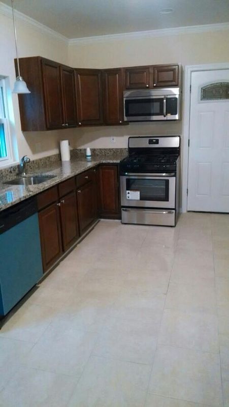 Empty kitchen with dark wood cabinets, stainless steel appliances, and a light tile floor.