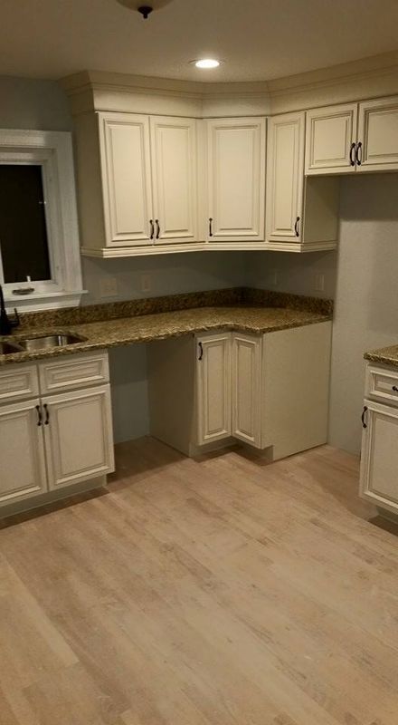 Empty kitchen with cream cabinets, brown countertops, and light wood flooring.