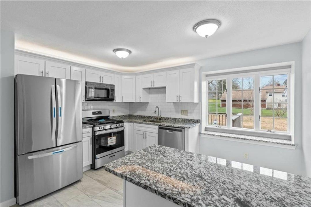 Bright modern kitchen with stainless steel appliances, white cabinets, and speckled granite countertops.