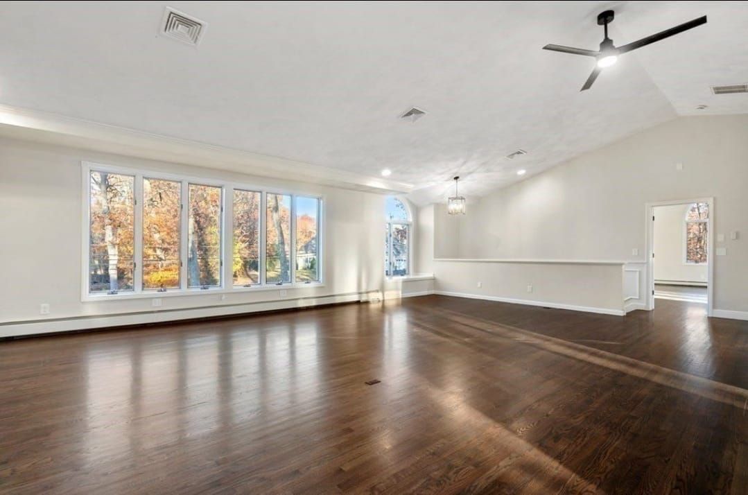 Bright empty living room with dark wood floors, white walls, large windows, and a ceiling fan