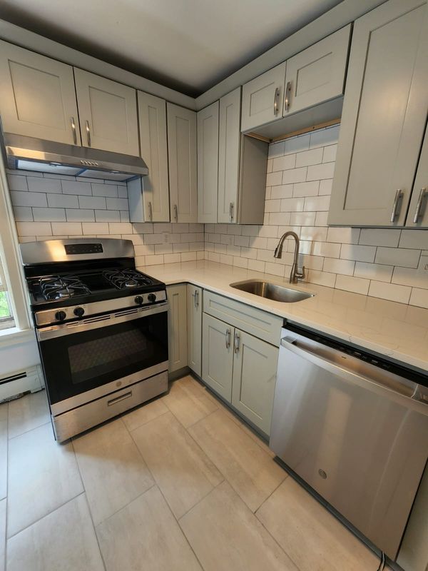 Compact white kitchen with stainless steel stove, sink, dishwasher, and subway tile backsplash