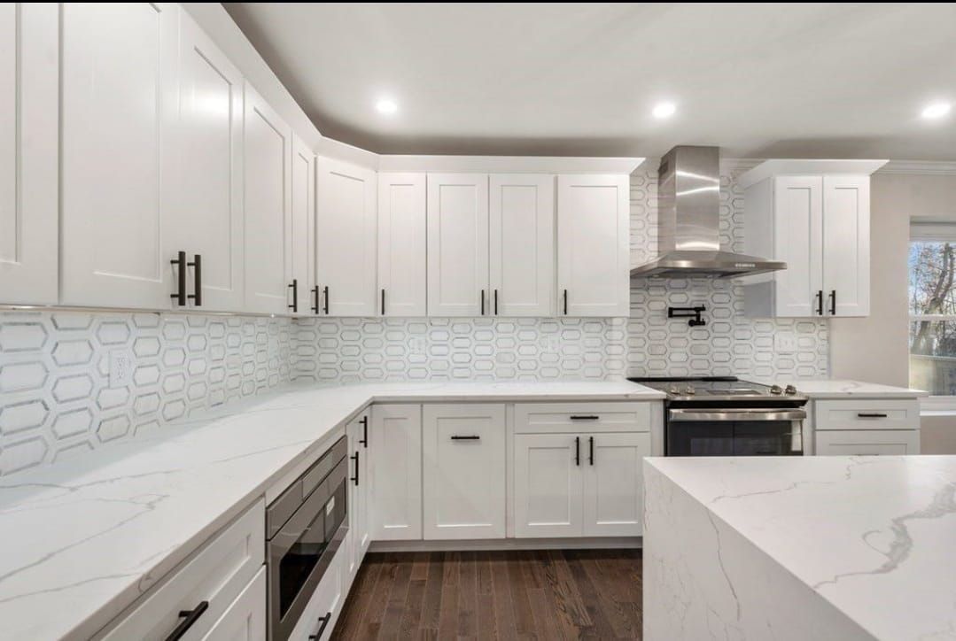 Bright white modern kitchen with marble countertops, white cabinets, stainless appliances, and dark wood floor
