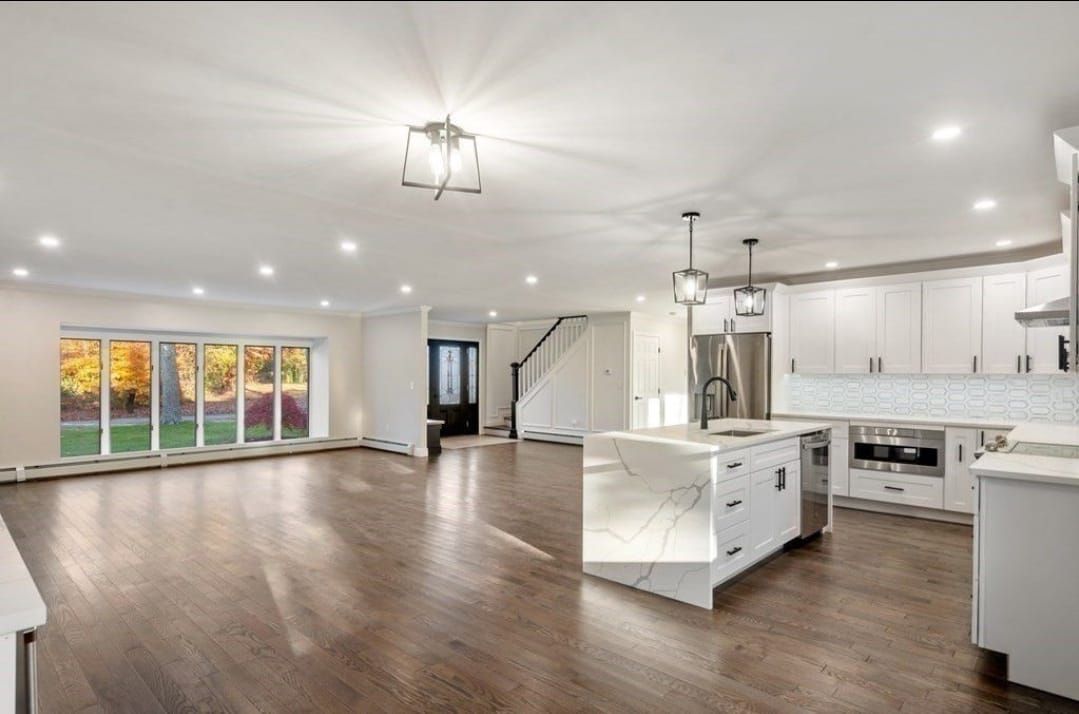 Bright open-concept kitchen and living room with white cabinets, dark wood floors, and large windows.