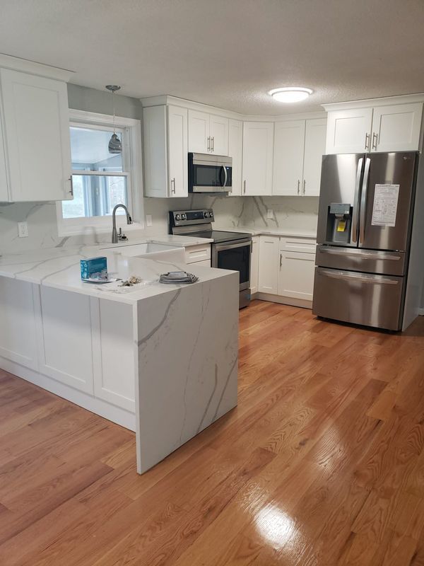 Bright white kitchen with marble island, stainless steel appliances, and hardwood floors