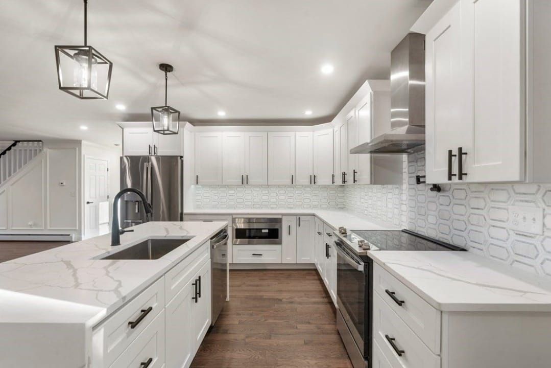 Bright modern white kitchen with island, pendant lights, stainless steel appliances, and wood flooring