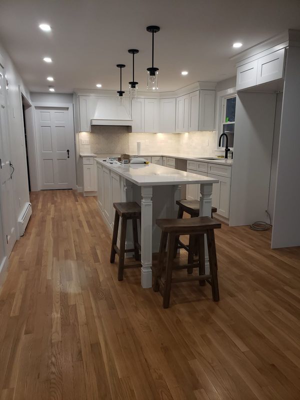 Modern white kitchen with island, pendant lights, hardwood floor, and two stools