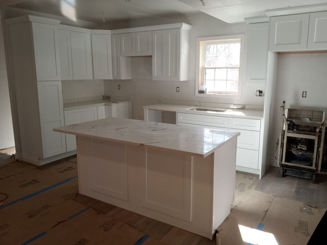 Bright white kitchen under renovation with island, cabinets, and covered floor