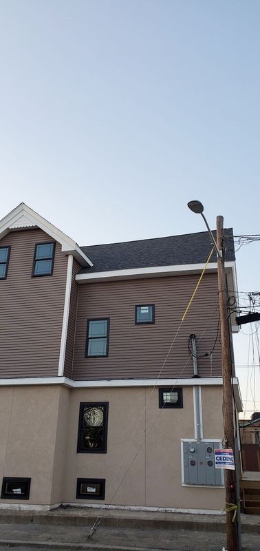 Residential house exterior with beige siding, dark roof, small windows, and a streetlight pole in front