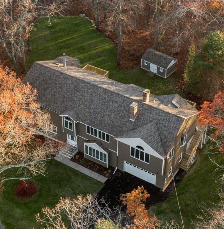 Aerial view of a tan house with gray roof, surrounded by trees and a green lawn.