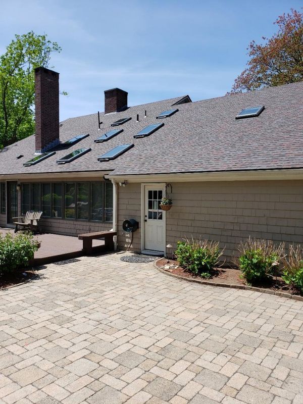 Brick-paver patio outside a beige house with skylights, chimney, and a back door under a clear blue sky