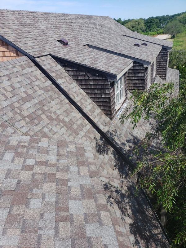 Roof with multiple dormer windows and gray shingles on a steep hillside house