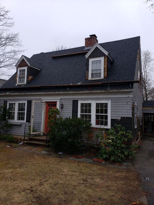 Gray two-story house with dormer windows, white trim, and a red front door on a cloudy day