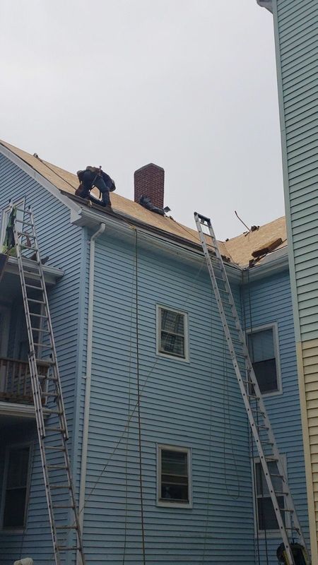 Workers repairing roof on a blue house with two ladders and a brick chimney