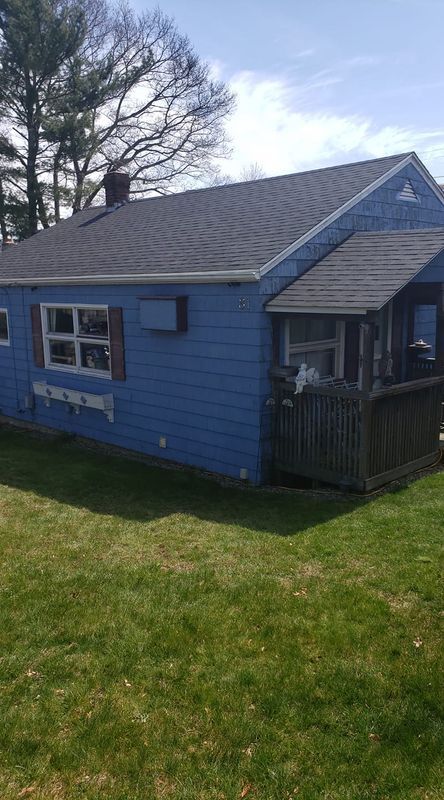 Small blue house with gray roof, front porch, and grassy yard under a cloudy sky