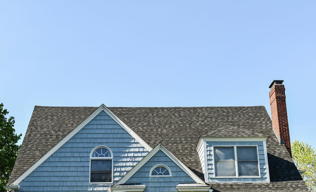 Blue house gable roof with white-trimmed windows and a red brick chimney under a clear sky
