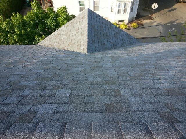 Rooftop with gray shingles and a small peaked vent, overlooking trees and buildings below
