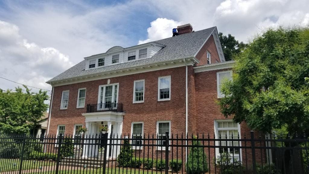 Red brick house with white trim and black iron fence under a cloudy sky