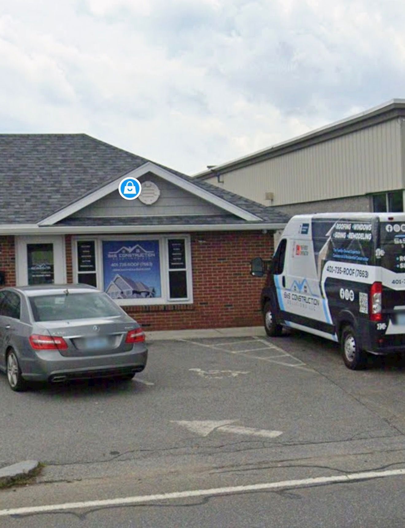 Small brick storefront with a blue sign, parked silver car, and white work van in front.
