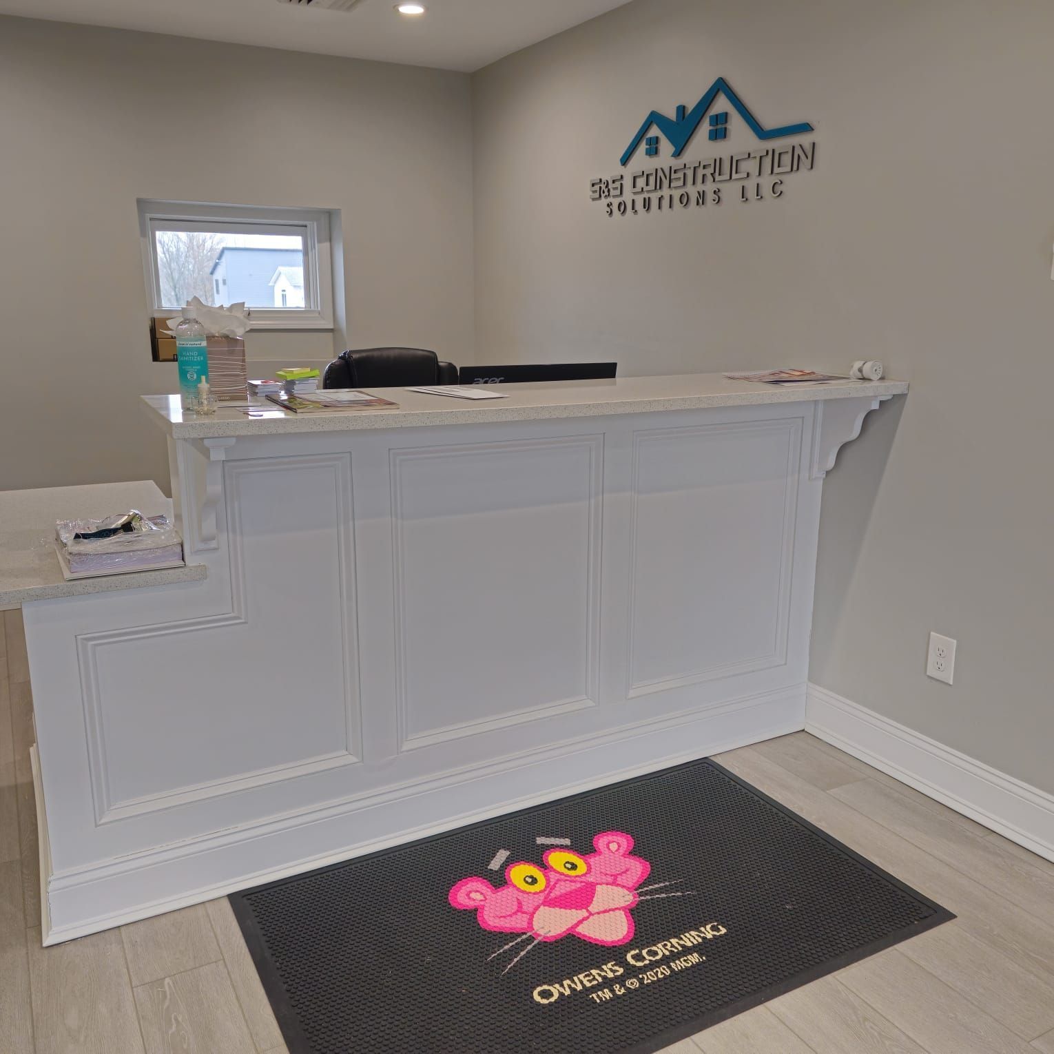 Empty reception desk with a white counter, black logo floor mat, and wall sign in a small lobby