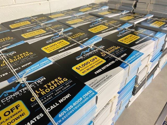 Stack of glossy black and blue trade show brochures with yellow promo labels on a table