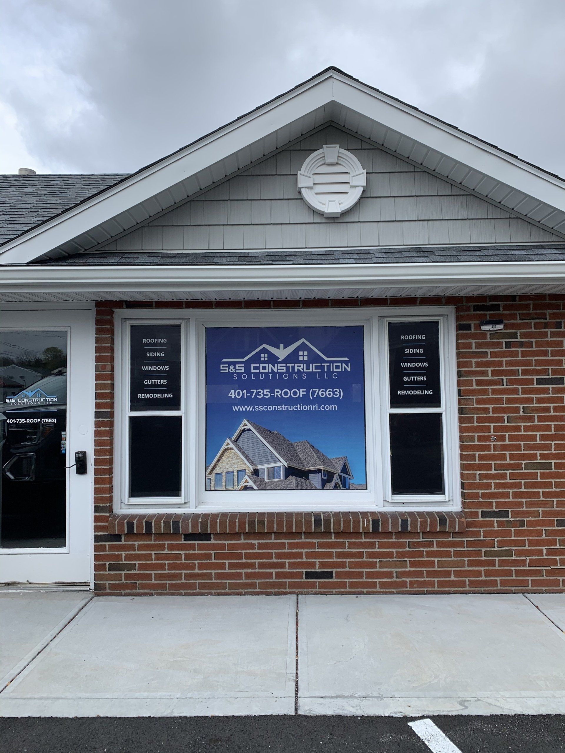 Storefront with brick facade, white trim, and a large blue window sign under a gabled roof