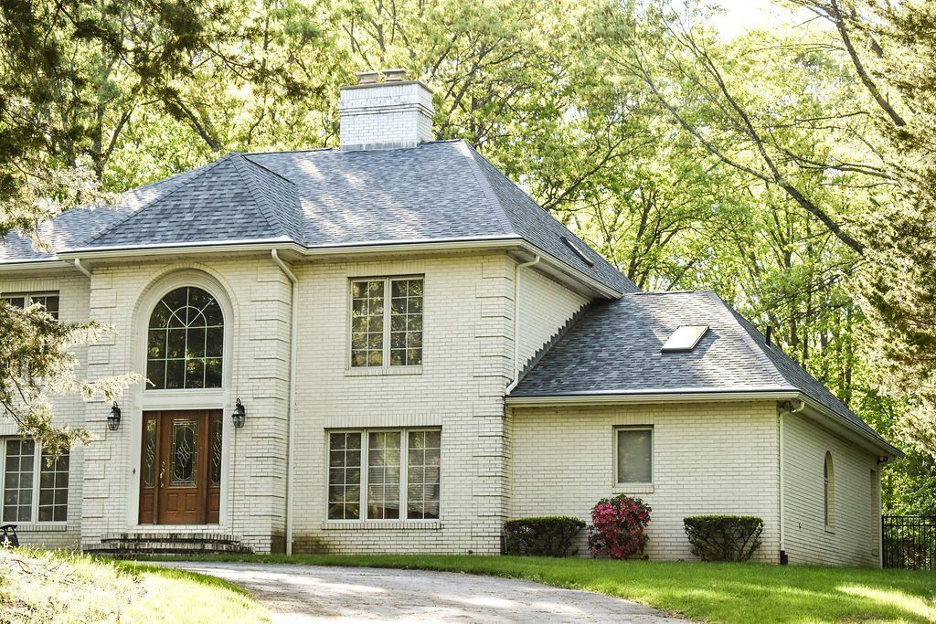 White two-story house with arched windows and a front porch, surrounded by trees and greenery