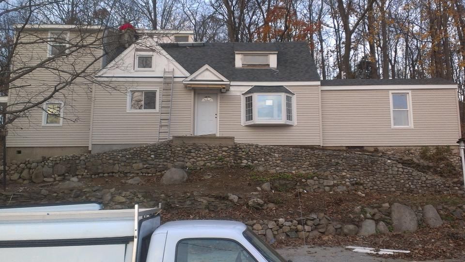 Beige house on a rocky hillside with a white truck partially visible in the foreground.