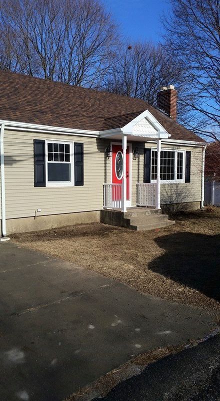 Single-story beige house with black shutters, a red front door, and a small porch on a sunny day