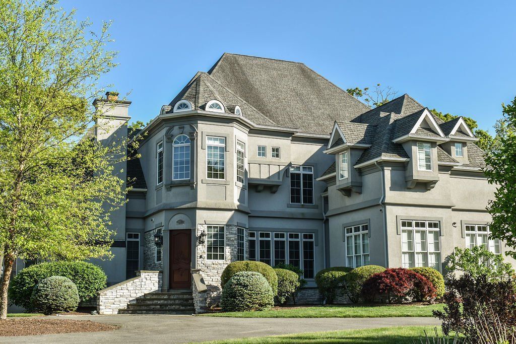 Large gray stone house with a steep roof, front steps, and landscaped yard in daylight