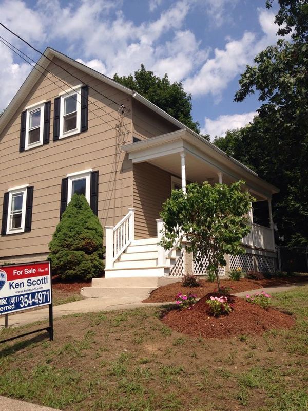 Two-story beige house with white porch and a red for sale sign in front