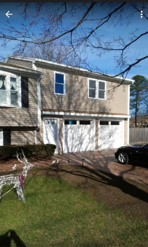 Two-story beige house with white garage doors, a driveway, and a small front lawn under a blue sky