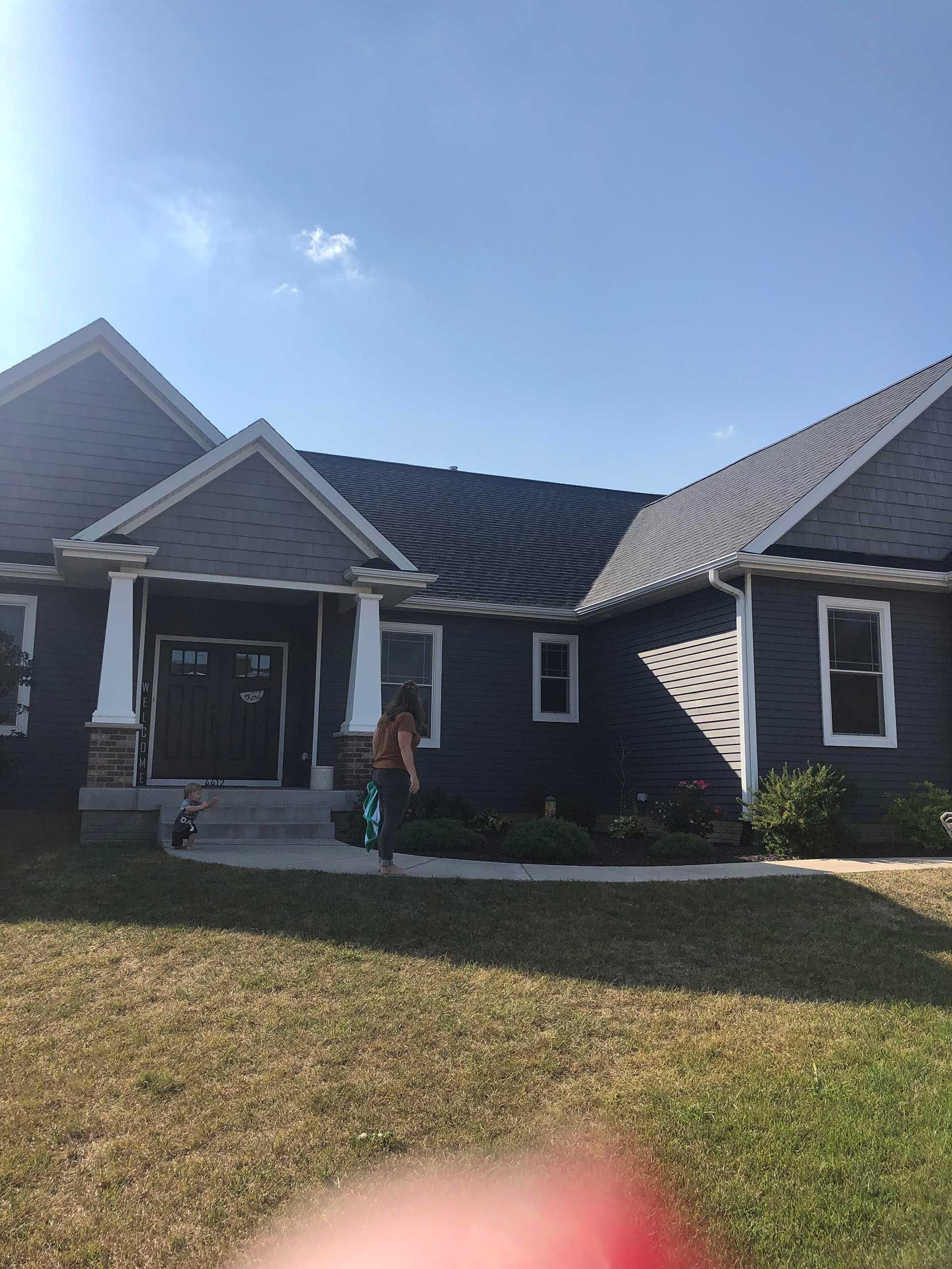 A dark blue house with white trim and a person in the doorway. Blue sky in the background.