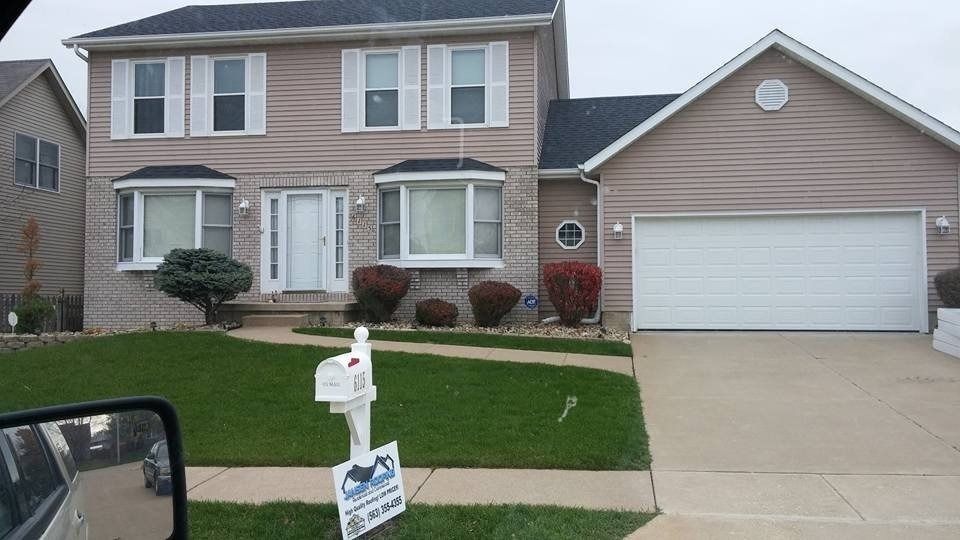 Two-story house with beige siding, white garage door, and a green lawn.
