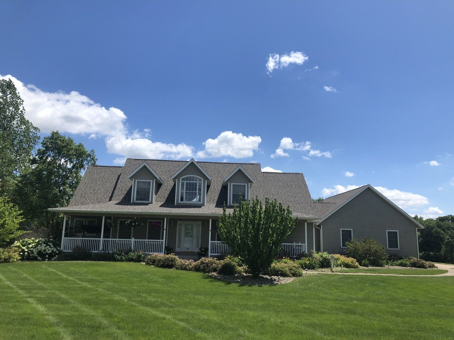 House with gray siding and roof, front porch, and dormers under a blue sky.