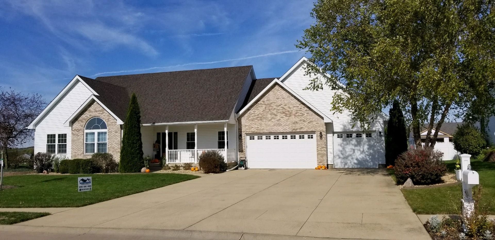 A house with white siding, a gray roof, and a concrete driveway on a sunny day.