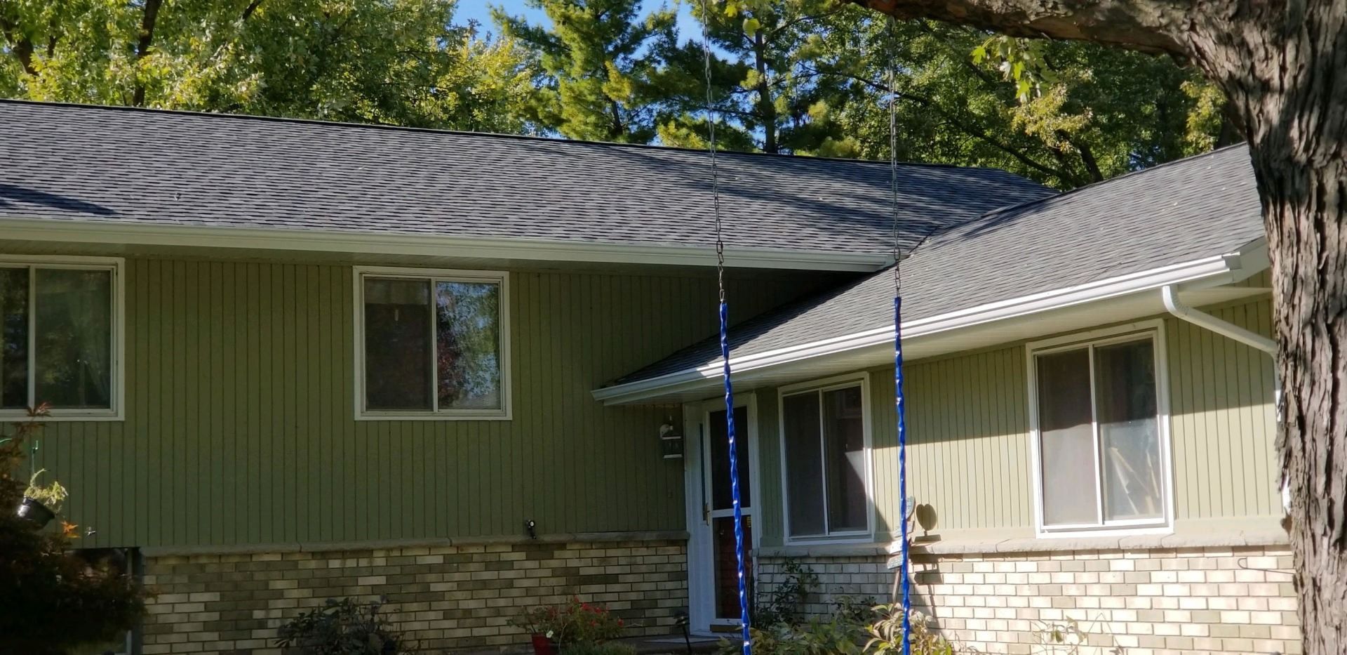 A light green house with gray roof, windows, and brick base. A blue ladder leans against the building.