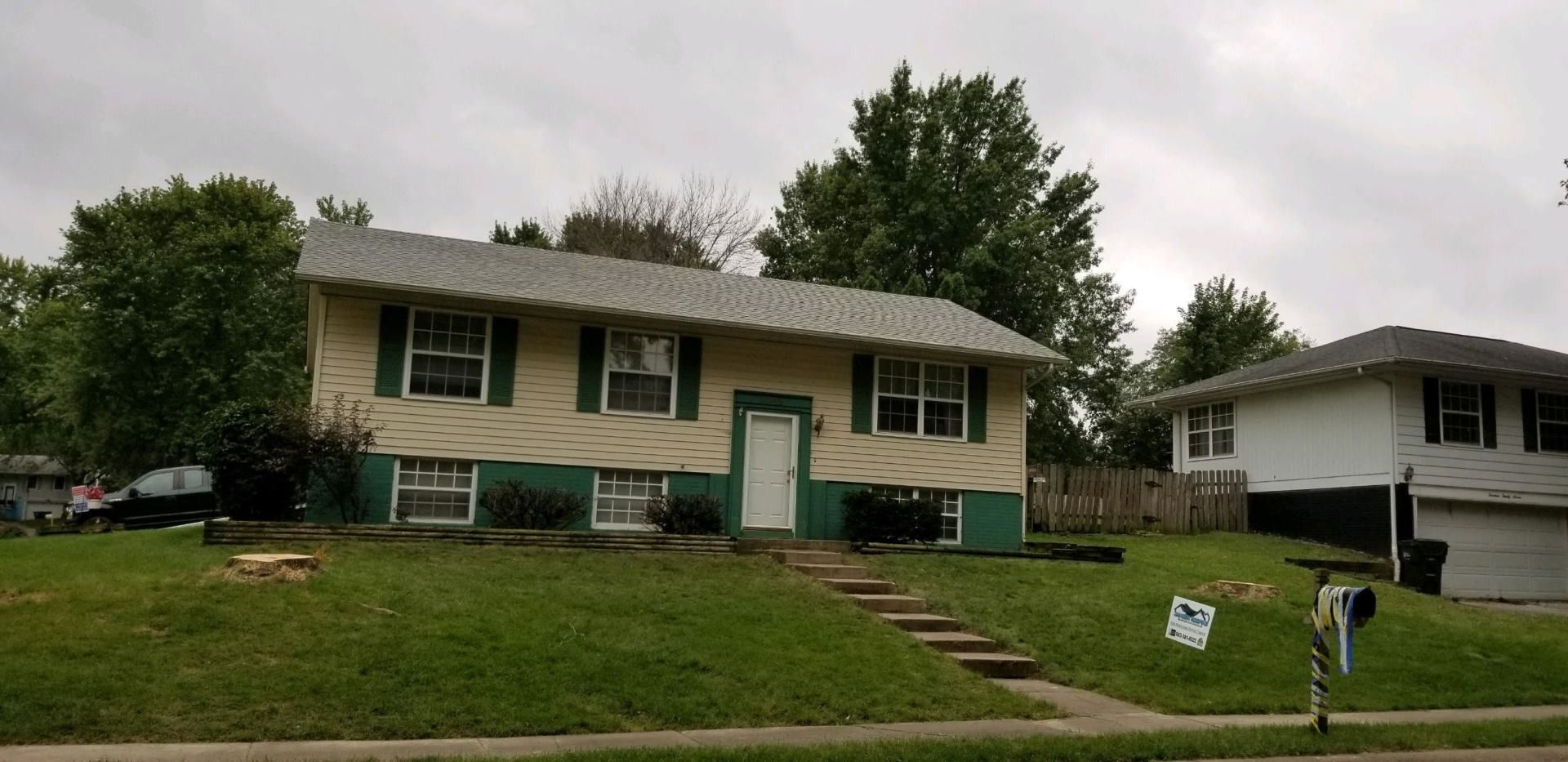 Split-level house with green trim, green shutters, and a green front yard. A cloudy sky is overhead.