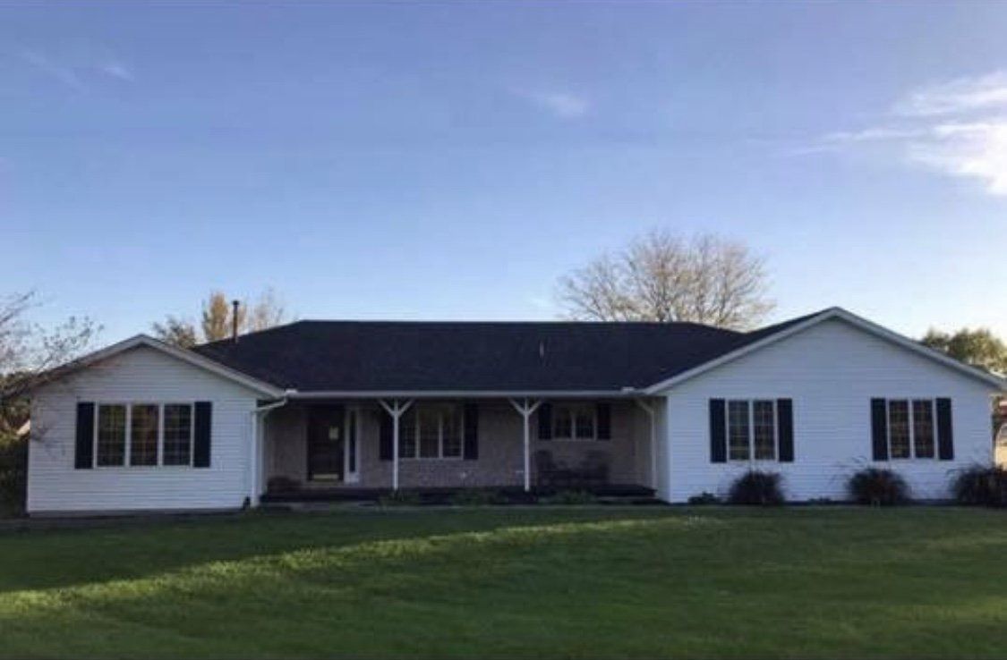 White ranch house with a dark roof and black shutters, set in a grassy yard under a blue sky.