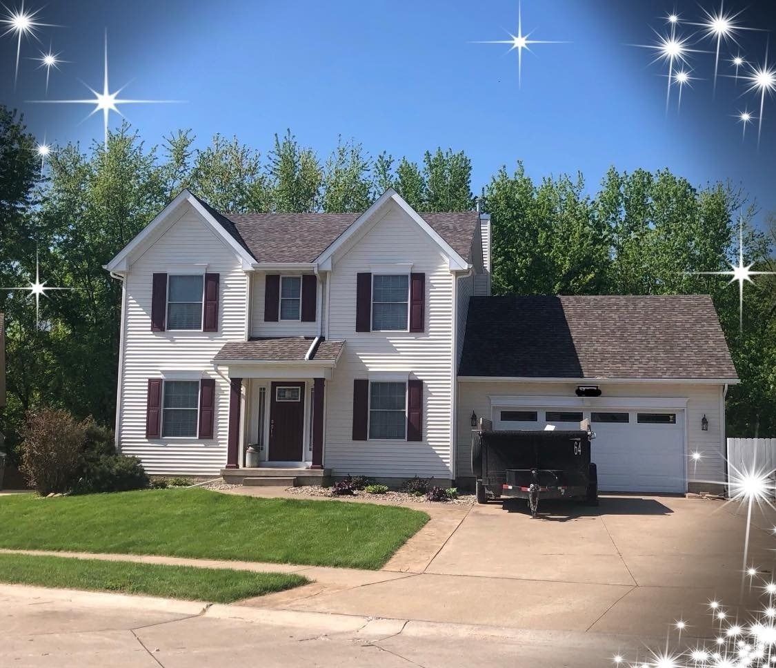 White two-story house with dark red shutters, a lawn, and a driveway with a trailer.
