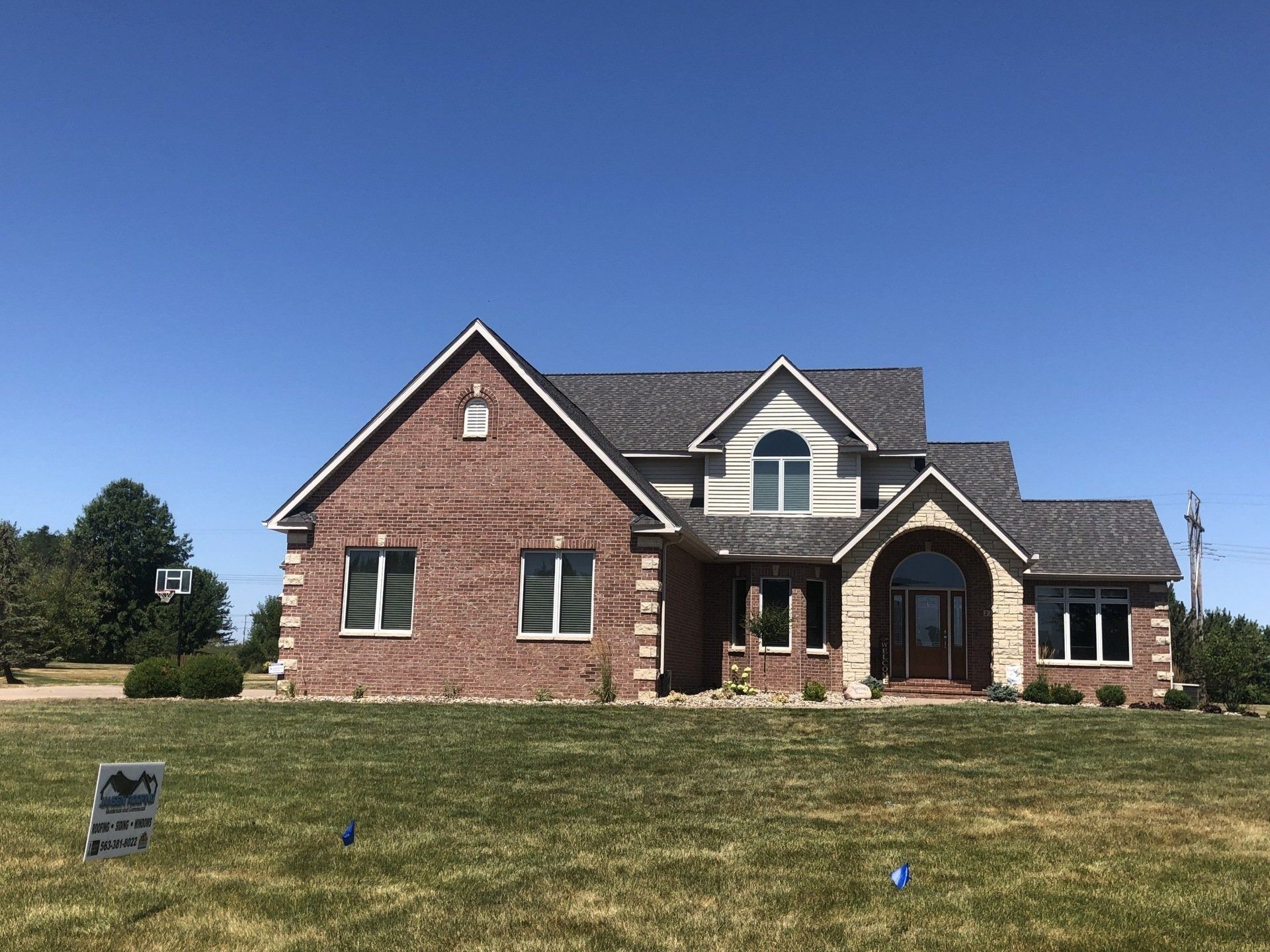 Red brick house with stone accents, arched entryway, and gray shingled roof under a blue sky.