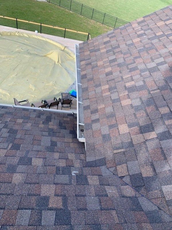 Brown and gray shingle roof with a gutter, overlooking a backyard with a covered pool.
